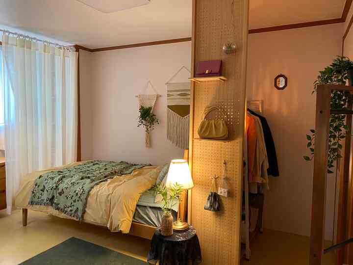Natural pastel-toned bedroom with wood tones featuring a bed with mattress, table lamp, and plants creating a cozy atmosphere