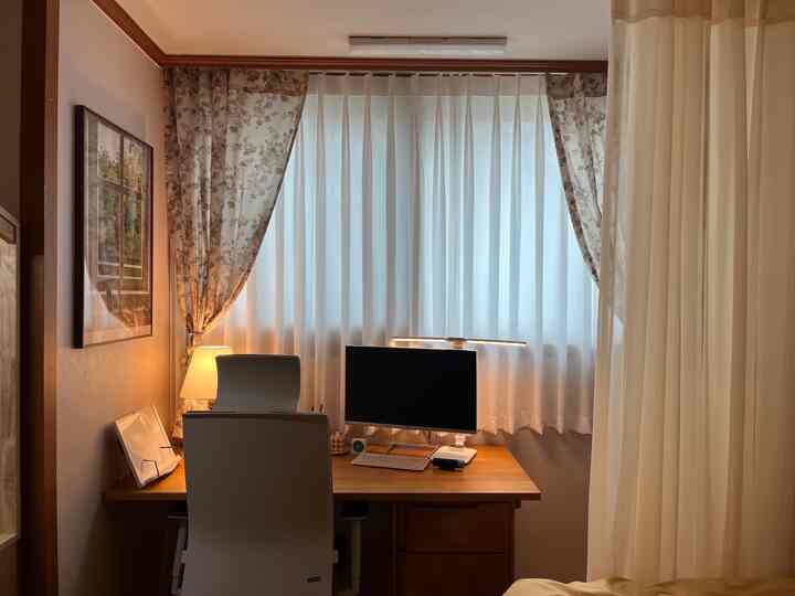 White and wood tone small bedroom-style home office space featuring curtains and desk setup