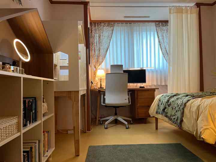 Yellow and white toned bedroom and home office space featuring wooden desk and office chair with a cozy atmosphere