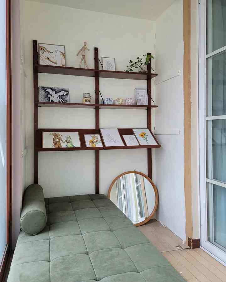 Natural tone veranda featuring a green sofa bed and wall-mounted shelves displaying artworks in a cozy setting