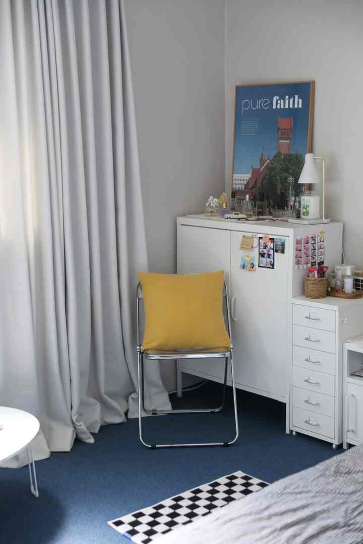 ホワイトの壁とブルーのタイルカーペットが敷かれたベランダ風の空間、黄色いクッションが置かれた金属製の椅子と白い引き出しキャビネットが配置された雰囲気のあるインテリア