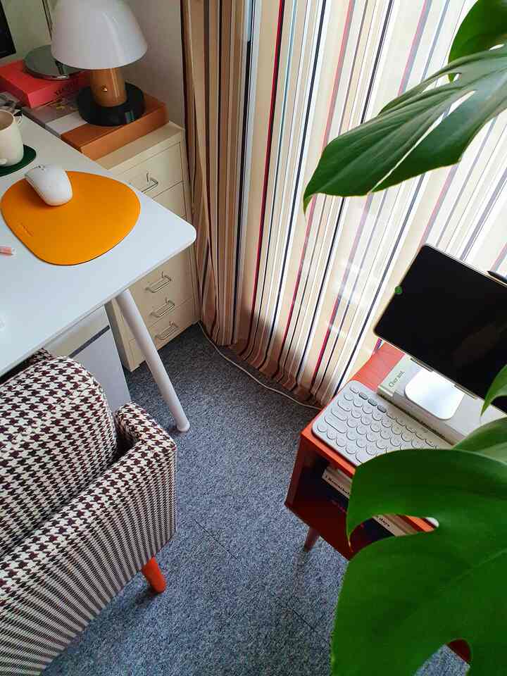 Natural-toned small home office with gray carpet and striped curtains, featuring a white desk and houndstooth office chair