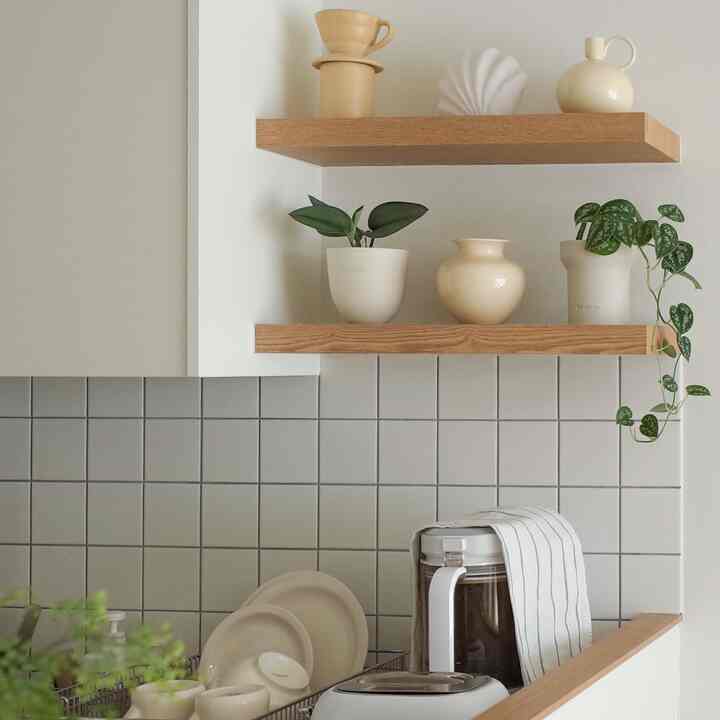 ナチュラルなウッドトーンの棚とホワイトベージュのキッチンタイル、様々な花瓶や植物が配置された雰囲気のあるキッチン空間