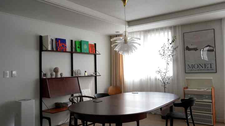 A white-walled dining room with brown wood furniture featuring a Louis Poulsen pendant lighting creating cozy atmosphere