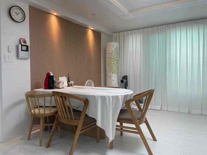Living room dining area with white base and wood tone furniture, featuring chiffon curtains and wooden chairs creating a cozy atmosphere