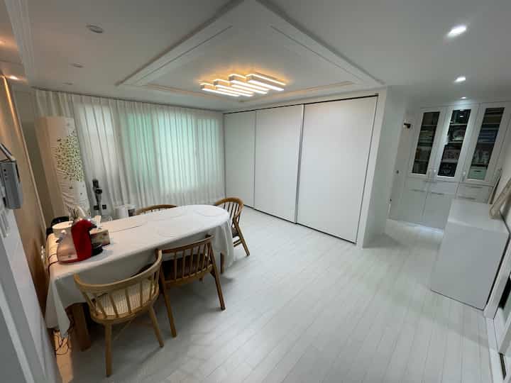 Bright white-toned living room featuring wood-toned dining chairs and built-in closets with a clean, minimal design