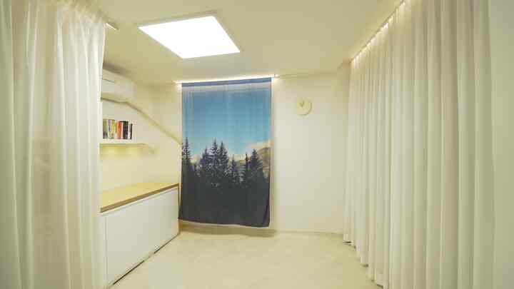 Bright white-toned studio apartment featuring clean white cabinetry and a blue forest-patterned curtain with modern minimal ambiance