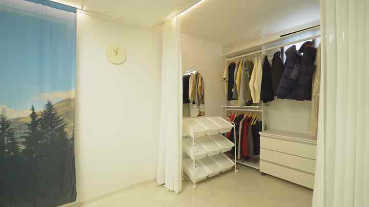 明るいホワイトとウッドトーンのウォークインクローゼット、白いカーテンと整然とした衣類収納が配置された空間