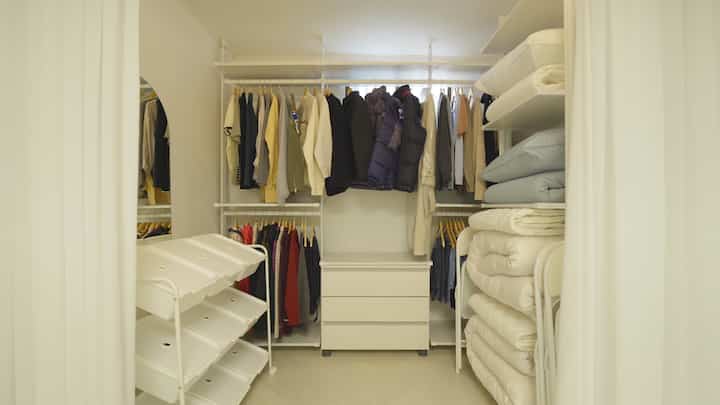 White-toned walk-in closet featuring metal hangers, dresser, and organized storage in a minimal interior space