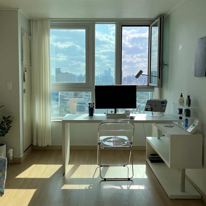Bright home office in natural light with white tones, featuring a transparent chair and computer setup for a clean workspace