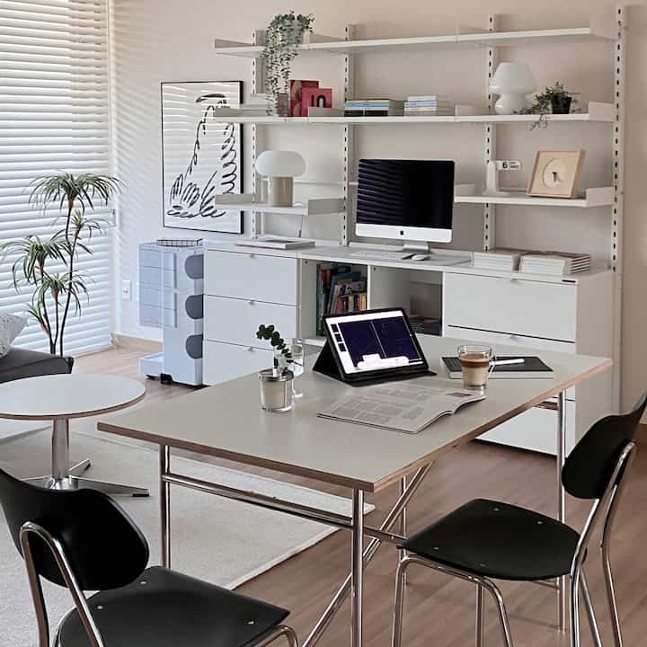 White and wood tone living room home office featuring simple modern desks, chairs, and system bookshelves in a bright setting