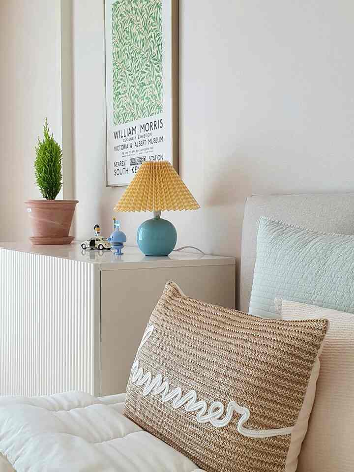 暖かいベージュとミント色のアクセントがある子供部屋、枕とクッションのあるベッドと小さなランプが配置された印象的な空間