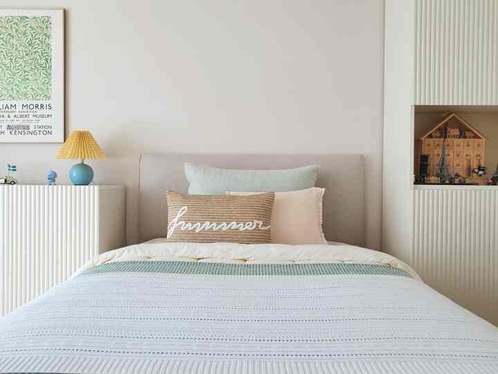Cream and white toned bedroom with central bed and cushions, flanked by storage cabinets, neat and simple space