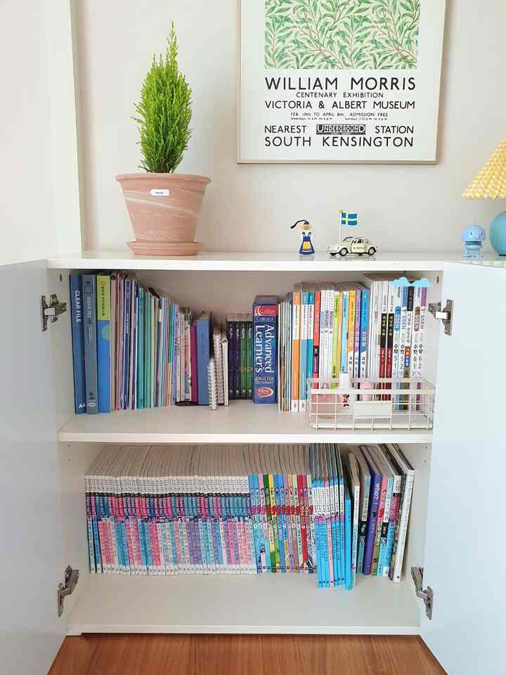 白い収納棚が中央に配置された子供部屋、整頓された本とウィリアム・モリスのポスター、鉢植えの植物がある印象的な空間