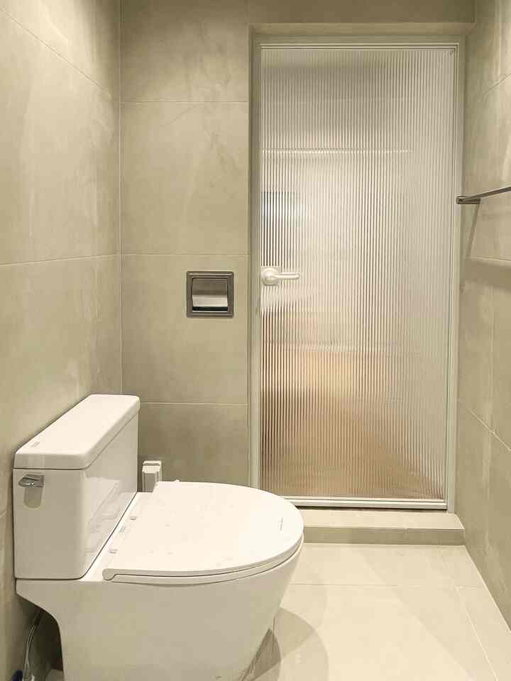 ベージュとホワイトの色調のバスルーム、清潔感のあるトイレと半透明のドアが配置された雰囲気のあるインテリア