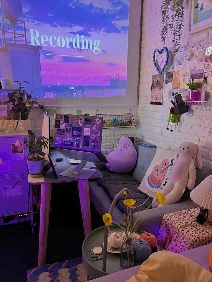 Compact home office space with purple lighting, gray sofa, desk, and projector screen creating a cozy atmosphere
