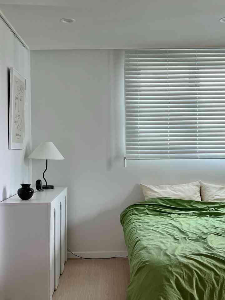 Simple modern bedroom dominated by white and wood tones featuring a bed and storage cabinet in a compact space with a calm atmosphere
