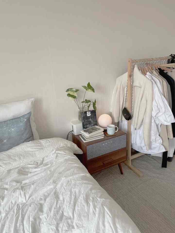 Bright white and wood tone bedroom featuring a nightstand and clothes rack with a clean, natural atmosphere
