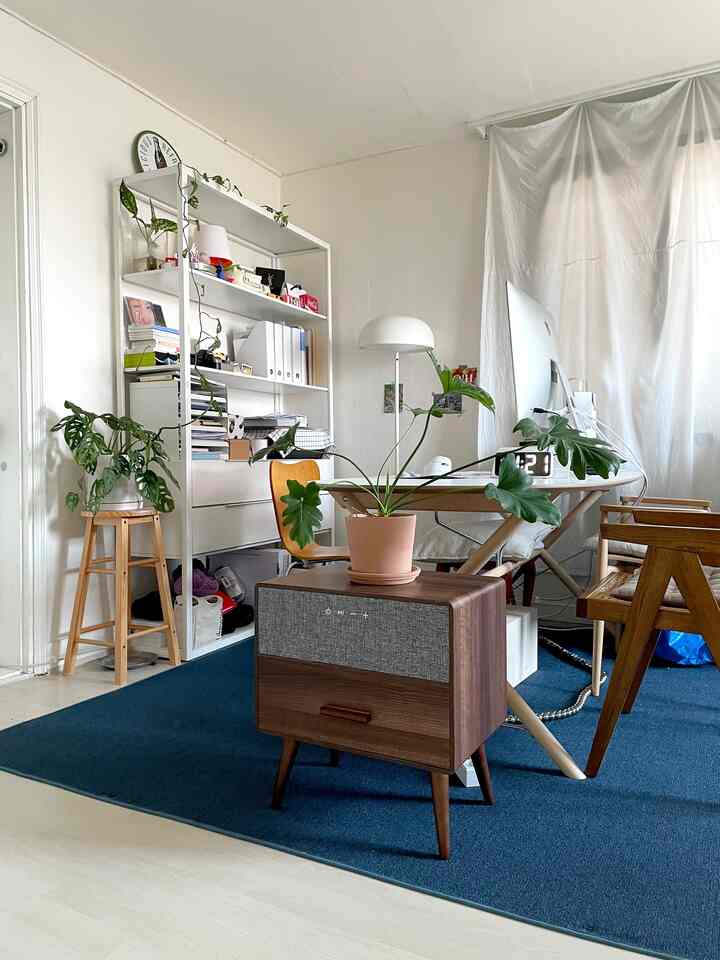 白い壁と木目調家具が調和した北欧風リビング、デスクとサイドテーブルには植物や電子機器が配置された雰囲気のある空間
