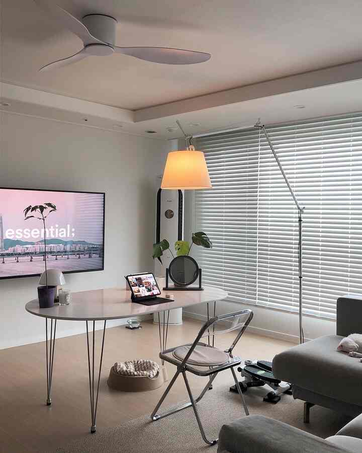 White and beige toned living room featuring Artemide Tolomeo floor lamp, large oval table, and transparent folding chair in a modern tidy space