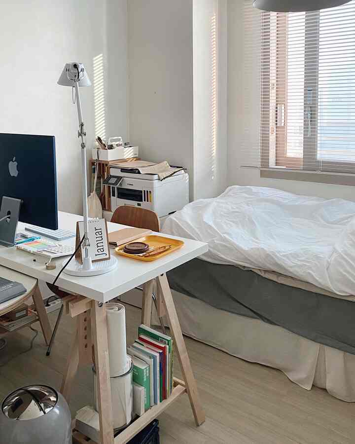 A compact bedroom and home office in white and natural tones, featuring a desk and bed arranged for efficient use of space