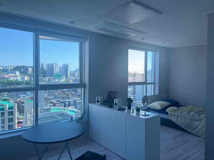 モノトーンとホワイトカラーのワンルーム寝室兼ホームオフィス、広い窓から公園の景色が見える雰囲気のあるインテリア