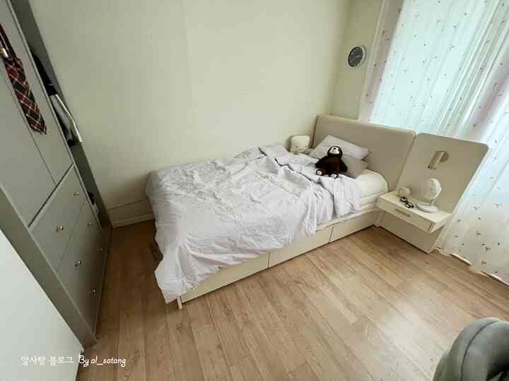 Small bedroom featuring white and wood tones, with a bed, wardrobe, and window curtains arranged in a simple design