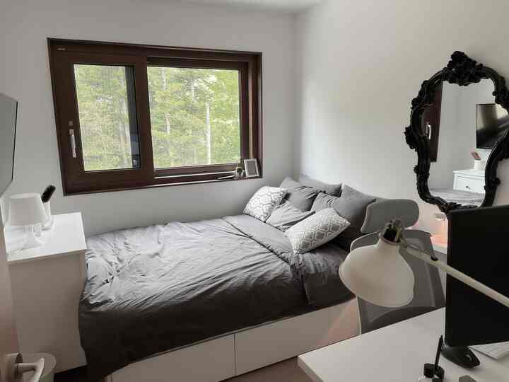 Small bedroom in white and gray tones featuring a wooden framed window, gray bed, desk and chair with a simple design