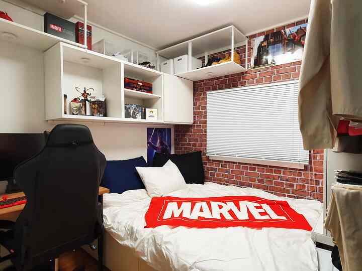 White and black toned single household bedroom featuring navy cushions and Marvel-themed gaming room elements with brick wall accents