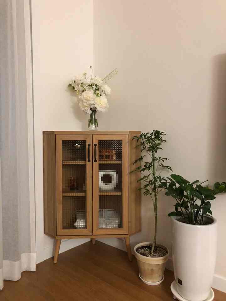 ナチュラルな色調のリビングのコーナー収納、透明なガラスの花瓶が配置された清潔で温かみのあるインテリア