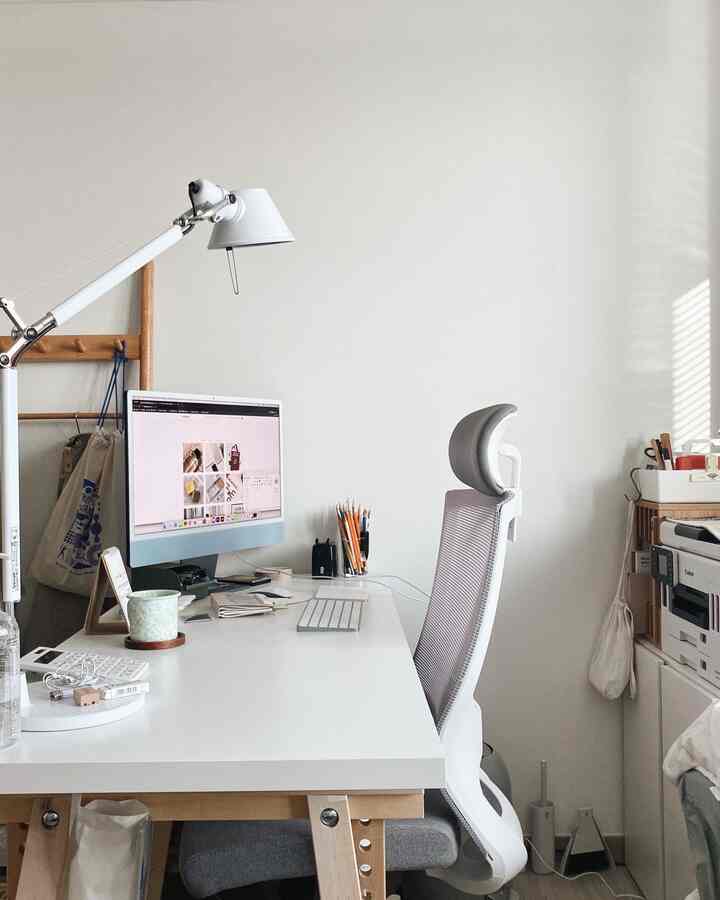 A compact white and wood-tone home office featuring a clean desk and ergonomic office chair with natural lighting