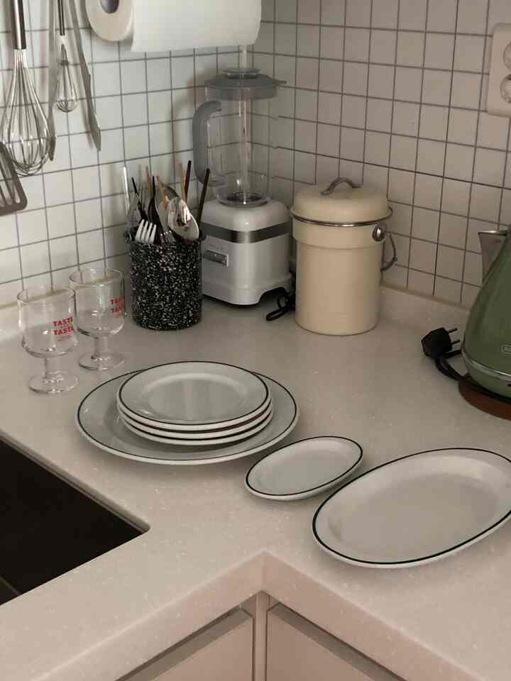Clean kitchen space with white tiled walls, kitchen utensils, and neatly arranged plates