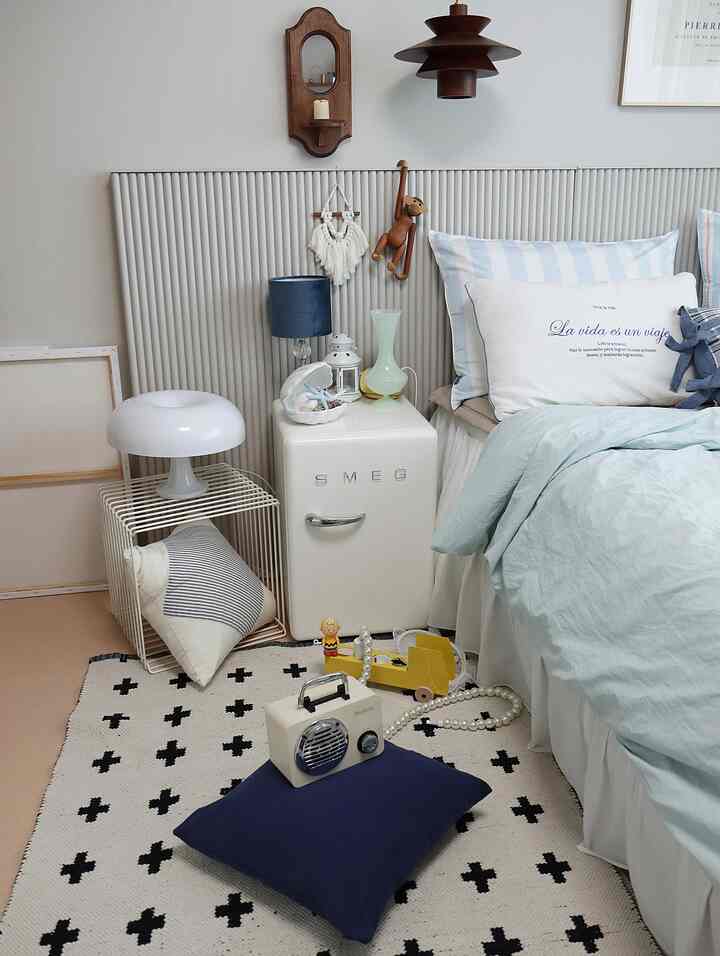 Bedroom in white and blue tones featuring a bed, a mini fridge, and vintage decorative items creating a cozy atmosphere