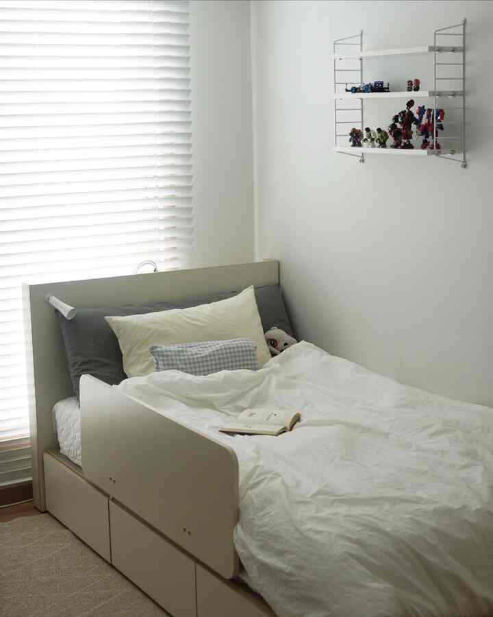 白い色調の子供部屋、ベッドとクッションが配置された落ち着いた印象の空間