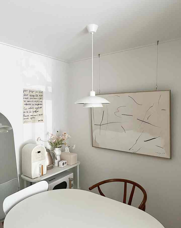 Bright white-toned kitchen space featuring an oval dining table, abstract poster, and compact kitchen appliances in a clean modern setting
