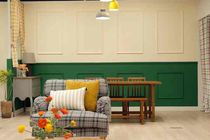 A cozy living-dining space with light ivory and deep green walls, featuring a wooden dining table, plaid sofa, and yellow cushions