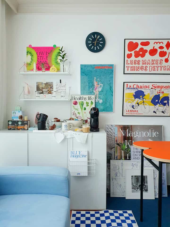 Bright and clean home cafe space with white walls and cabinet, blue sofa, and colorful framed posters