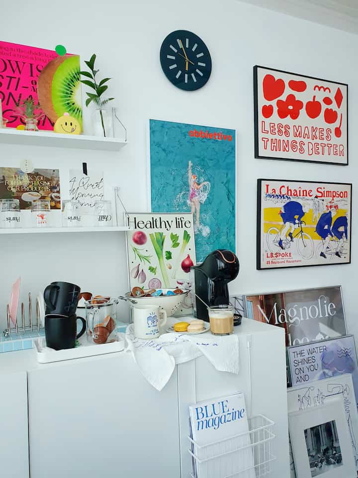 A white and black living room featuring a coffee machine, multiple picture frames, and posters for a cozy home cafe interior