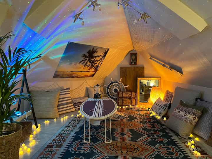 A cozy low-ceilinged 11-sided bedroom with a surfing-themed table, mood lighting, and cushions creating a warm resort atmosphere