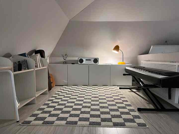 Modern music workspace with white and gray tones under a sloped ceiling, featuring an electronic piano and bookshelf arranged neatly