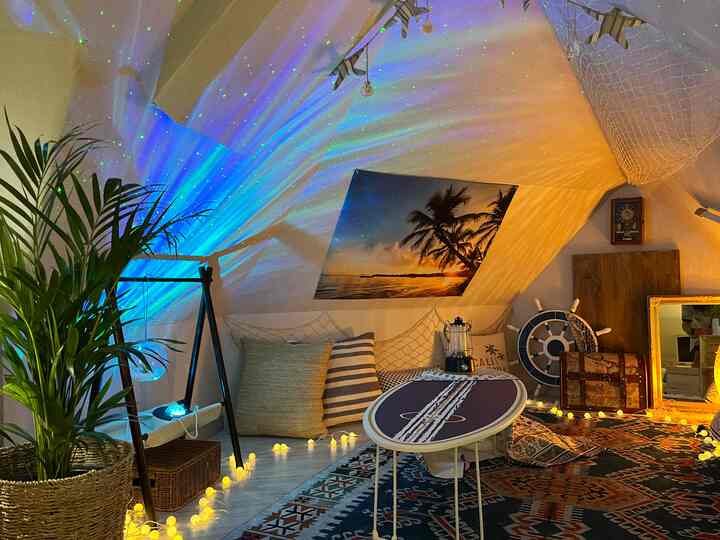 Natural beige-toned two-person hideaway featuring aurora lighting, surfboard table, and palm plant enhancing coastal ambiance