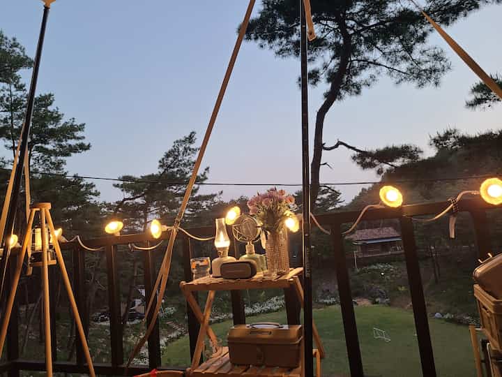 Wood tone balcony featuring warm string lights and a cozy camping-style table with natural outdoor scenery