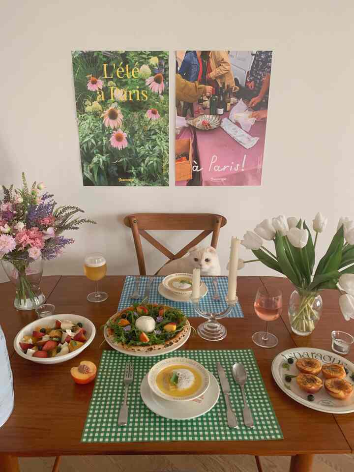 ナチュラルな色調のダイニングルーム、木製のテーブルと椅子があり、中央に猫が座り、花瓶とキャンドルが配置された雰囲気のある空間