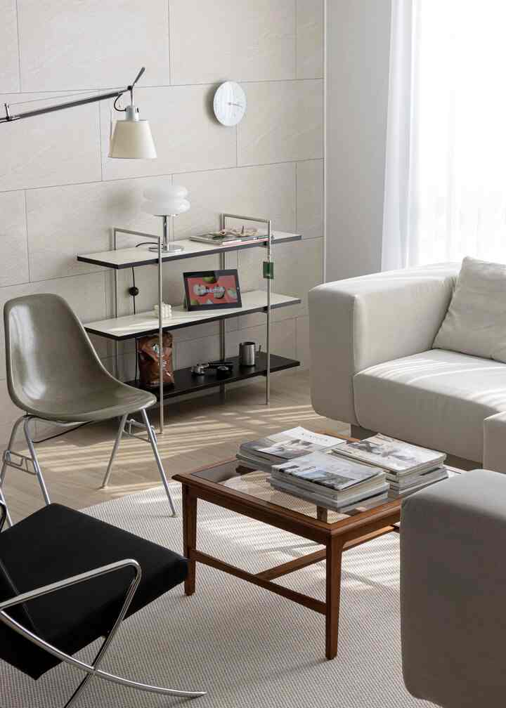 A softly lit living room in white and beige tones featuring a sectional sofa, wooden coffee table, and shelves in a simple modern style
