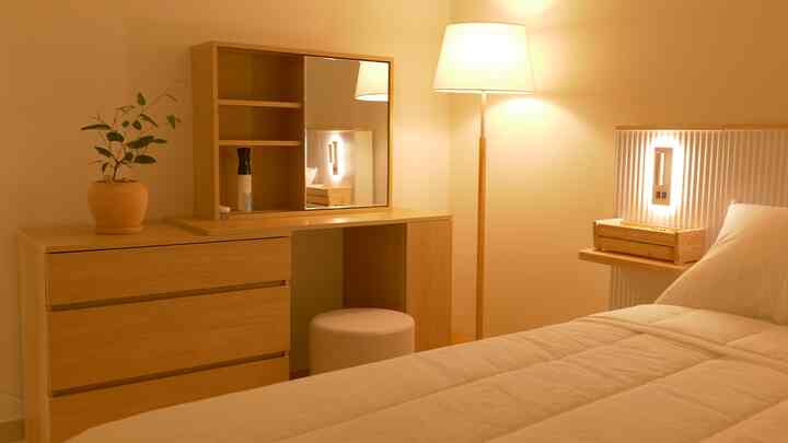 ナチュラルな木目調とベージュ色の寝室、化粧台とスツールが配置された雰囲気のあるホテルライクな空間