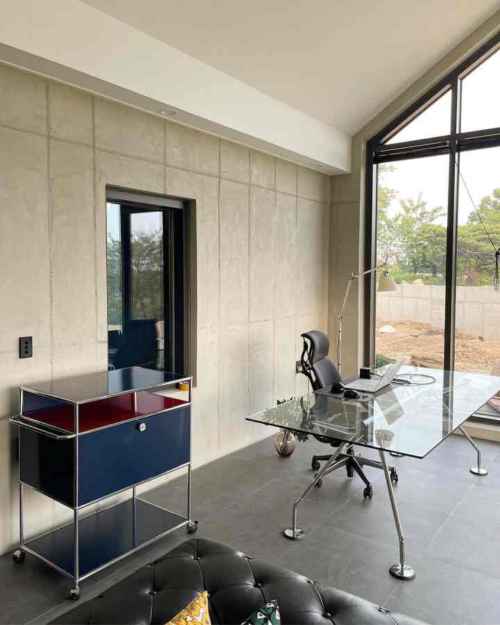 Modern living room and home office in gray tones, featuring a large window, glass table, and blue cabinet with a clean design