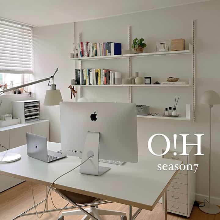 White-toned home office featuring a desk, bookshelves, and computers with a clean modern design