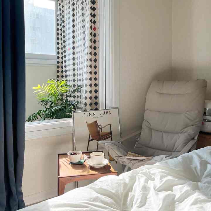 Bedroom with beige walls and navy curtains, featuring a gray armchair, wooden side table, and white bedding in a cozy natural modern style