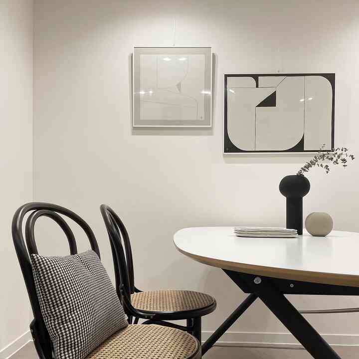 Clean two-person dining room in white and natural tones, featuring black framed wall art and a black vase as stylish accents