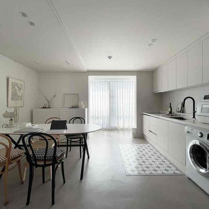 Modern kitchen space in white and black tones, featuring dining table and chairs with sheer curtains in a calm interior